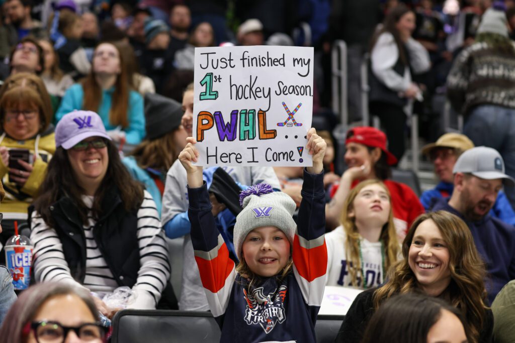 A young fan holds up a sign reading "Just finished my 1st hockey season, PWHL here I come!" at a PWHL 2025 Takeover Tour game in Detroit.