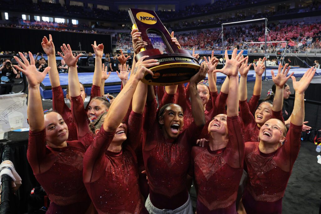 Oklahoma gymnast Danae Fletcher lifts the 2025 NCAA championship trophy with her teammates.