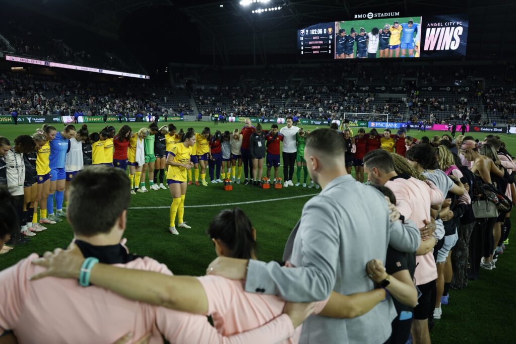 Utah's Alex Loera leads both Angel City and Royals players and staff in prayer for LA's Savy King on the field after an NWSL match.