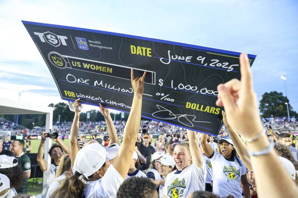 The US Women celebrate their second straight TST title while lifting their oversized 2025 $1 million check.