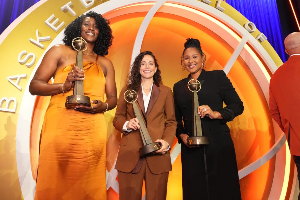 Retired WNBA legends Sylvia Fowles, Sue Bird, and Maya Moore hold their induction trophies at the 2025 Naismith Memorial Basketball Hall of Fame ceremony.