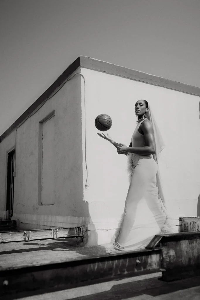 A black and white image of WNBA star A'ja Wilson tossing a basketball while walking by the outside of a building.