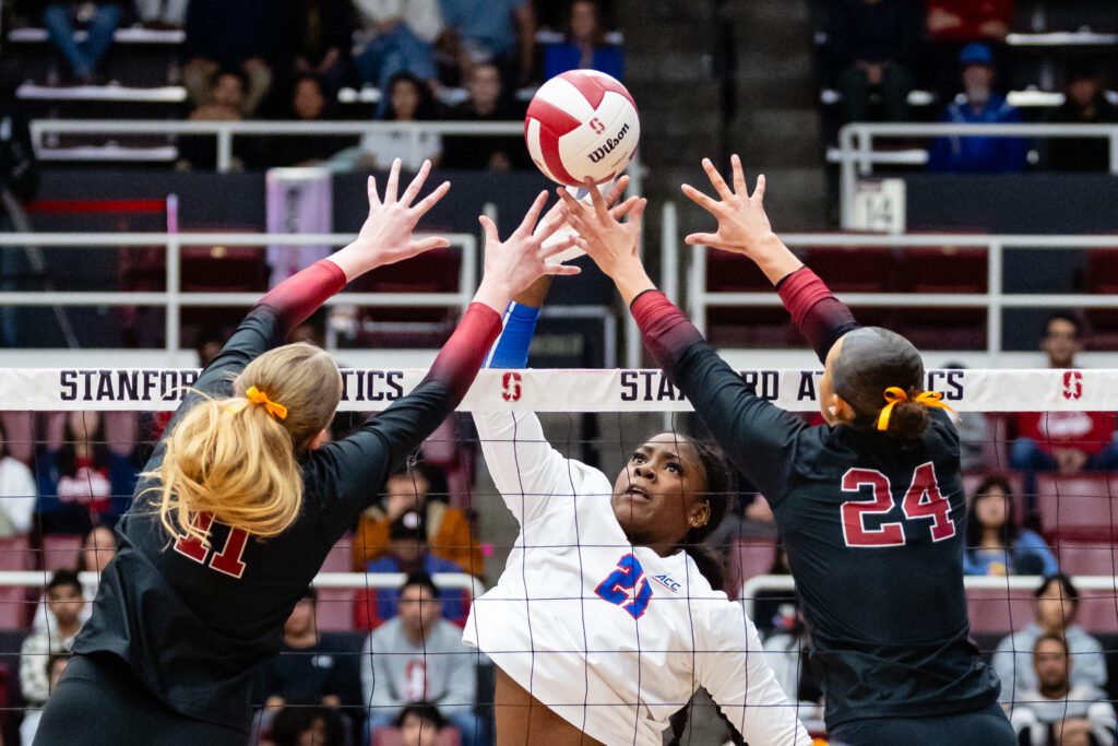 SMU middle blocker Favor Anyanwu aims to hit the ball through Stanford defenders' outstretched arms during a 2025 NCAA volleyball game.