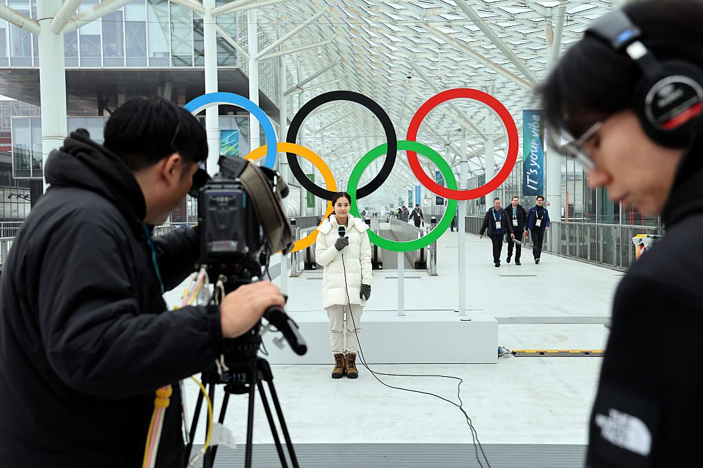 A camera crew films a reporter standing in front of the Olympic Rings outside the Fiera Milano exhibition centre, home of speed skating and hockey, ahead of the Milano Cortina 2026 Winter Olympics on February 01, 2026 in Milan, Italy. 