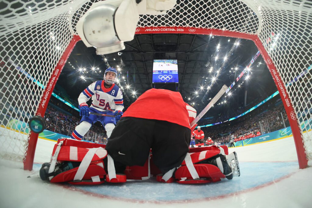 USA hockey forward Alex Carpenter flips the puck into the goal past Switzerland goaltender Andrea Brändli during a group-play game at the 2026 Winter Olympics.